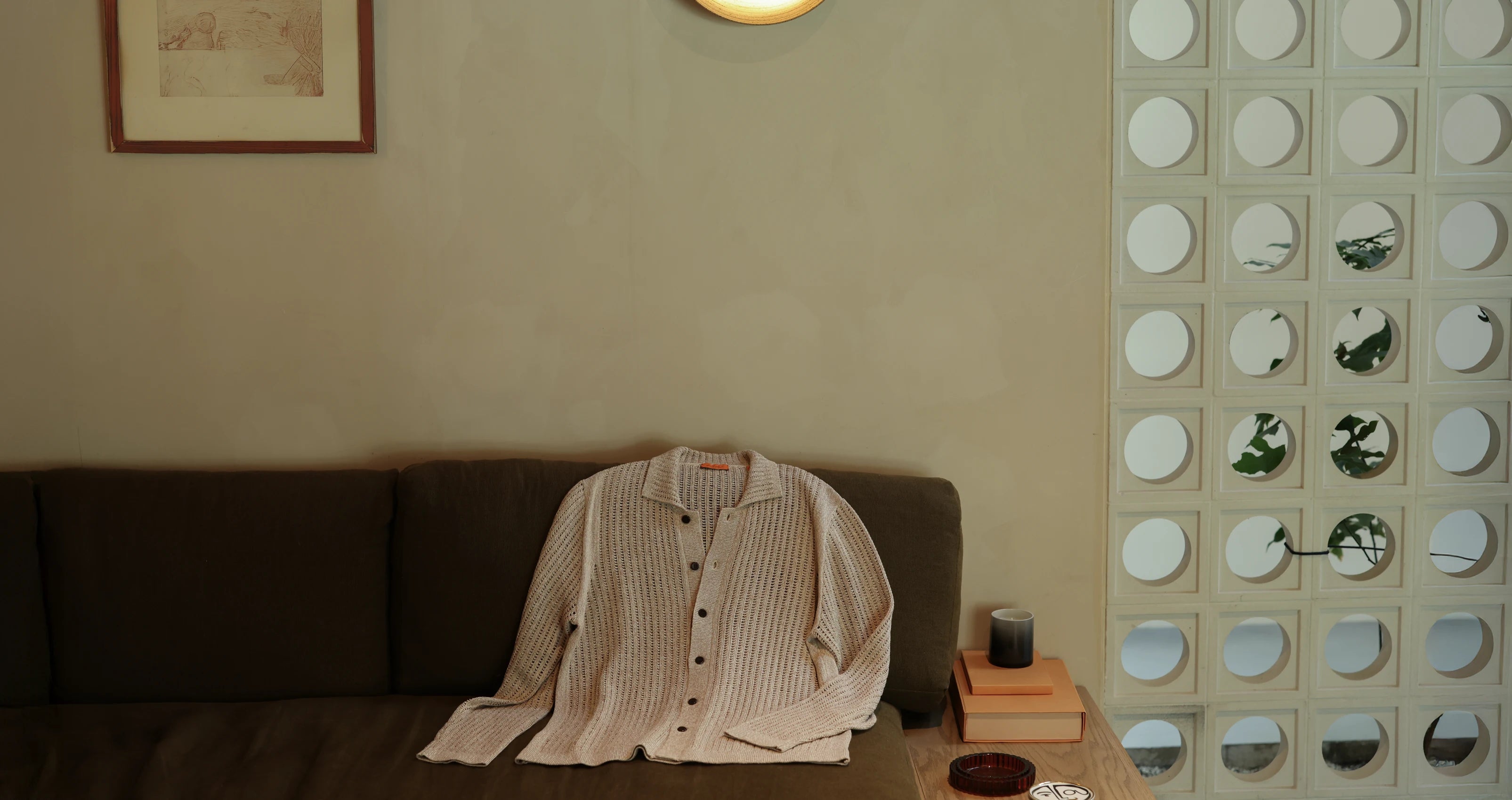 Uncle Purl Beige shirt on a dark brown sofa against a beige wall with a decorative mirror panel.