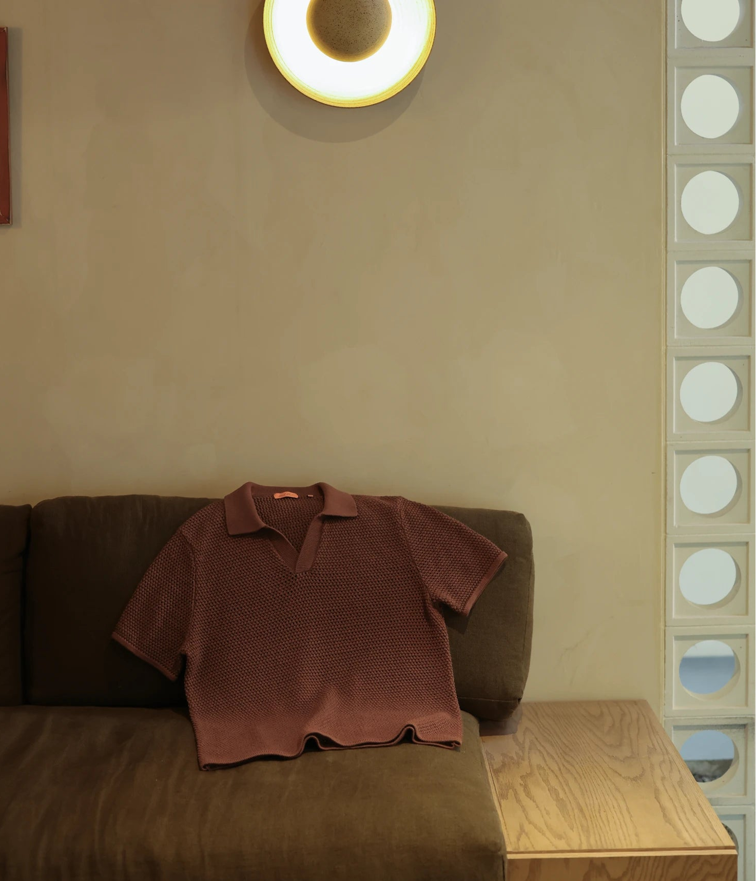 Brown polo shirt on a brown sofa with a beige wall and circular light fixture in the background.